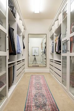 a walk in closet filled with lots of white shelves and drawers next to a rug