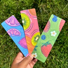 three handmade bookmarks in the shape of fruit are held up by someone's hand