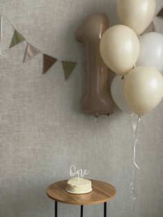 a cake sitting on top of a wooden table next to balloons and a number one sign