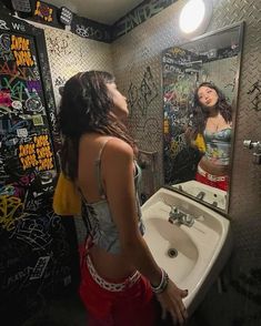 a woman standing in front of a bathroom mirror with graffiti on the wall behind her