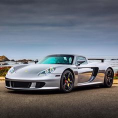 a silver sports car is parked on the side of the road near the ocean and rocks