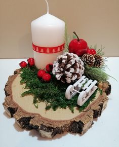 a white candle sitting on top of a piece of wood next to pine cones and berries