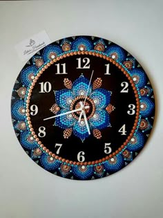 a blue and orange clock with numbers on it's face is hanging from the wall