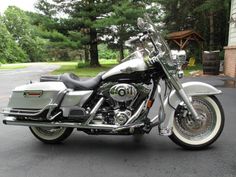 a silver motorcycle parked on the street in front of a house with trees behind it