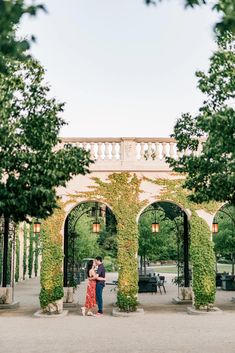 two people standing under an arch covered in green vines and ivys at the end of a walkway