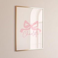 a pink bow is hanging on the wall next to a framed poster that says charlotte