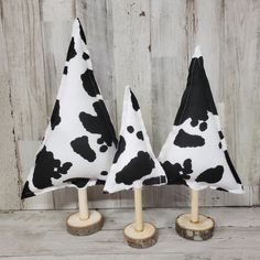 two black and white cow print christmas trees on wooden bases, one is made out of wood