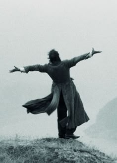 a man standing on top of a hill with his arms outstretched