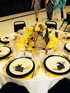 the table is set with black and white plates, silverware, and yellow flowers