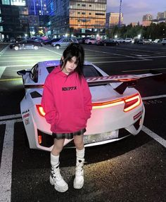 a woman standing next to a sports car in the middle of a city at night