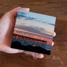 a person holding up a small photo of a pier at sunset with the sky in the background