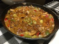 a skillet filled with meat and vegetables on top of a tablecloth covered counter