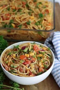 a white bowl filled with pasta salad next to a glass casserole dish on a wooden table