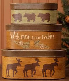 three wooden boxes with moose and bear designs on them, sitting next to a christmas tree