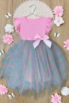 A charming rainbow tutu dress for girls from the SmileyWorld® x Mia Belle Girls collection, featuring a pink top with ruffled sleeves, a rainbow tulle skirt, and a pink bow, surrounded by floral decorations.