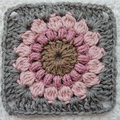 a crocheted square with a pink and gray flower on it's center