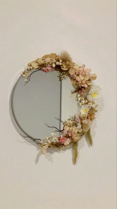 a round mirror with flowers on it hanging from the side of a wall next to a white wall