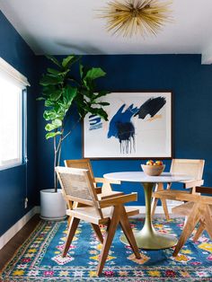 a dining room with blue walls and wooden chairs around a white table surrounded by potted plants