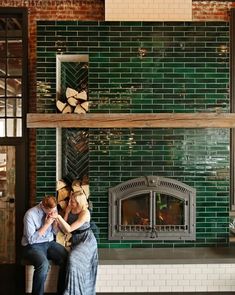 a man and woman sitting next to each other in front of a fireplace