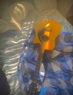 a yellow guitar laying on top of a blue and white checkered sheet covered bed