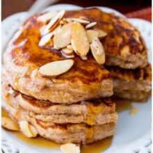 stack of pancakes with almonds and syrup on a white plate, ready to be eaten