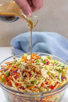 someone pouring dressing into a salad in a glass bowl