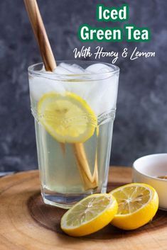 iced green tea with honey and lemon in a glass on a wooden tray next to sliced lemons