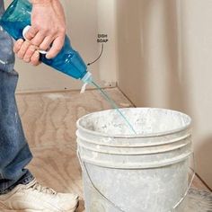 a man is pouring water into a bucket on the floor next to several pails