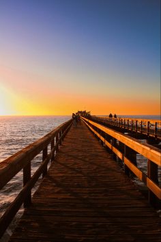 a long wooden pier stretches out into the ocean at sunset with people standing on it