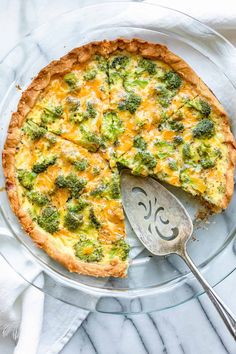 a quiche with broccoli and cheese on a glass plate next to a serving spoon