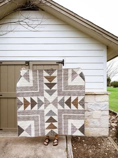 a woman standing in front of a garage holding up a quilt on the door way