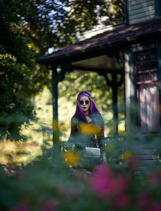 a woman with purple hair standing in front of a house