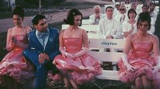 several people in pink dresses sitting on a bench with one man wearing a blue suit