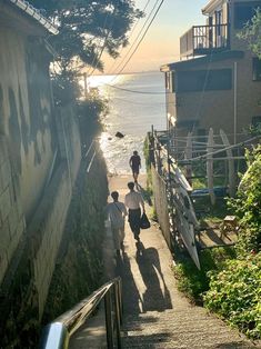 two people walking up the side of a steep hill next to an ocean and buildings