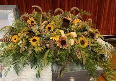 an arrangement of sunflowers, ferns and feathers in a vase on a table