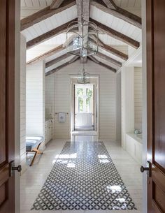 an open door leading to a bathroom with white walls and wood beams on the ceiling