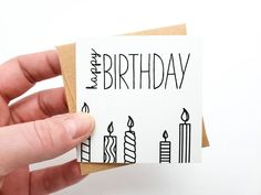 a hand holding a card with candles on it that says happy birthday in black ink