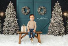 a little boy sitting on a bench in front of christmas trees