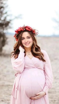 a pregnant woman in a pink dress poses for a photo while wearing a flower crown