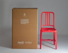 a red coca - cola chair next to a cardboard box on a grey background with an advertisement