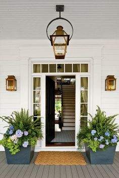 two large planters with blue flowers are on the front steps of a white house