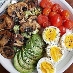 a white plate topped with eggs, tomatoes and cucumbers next to sliced avocado