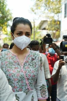 a woman wearing a face mask while standing in front of people with cameras around her