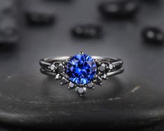 a blue sapphire ring sitting on top of a black stone surface with other stones in the background