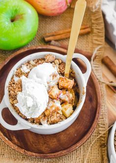 an apple crisp with ice cream in a bowl on a wooden plate next to apples and cinnamon sticks