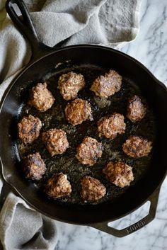 meatballs are cooking in a skillet on a table with napkins and cloth