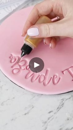 a woman's hand is writing on a pink plaque