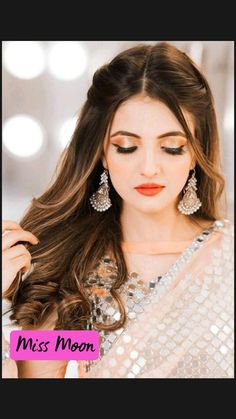 a woman with long brown hair wearing earrings and a white dress is posing for the camera