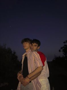 two young men standing next to each other at night with the moon in the background