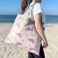 a woman walking on the beach carrying a pink tote bag with hedges all over it